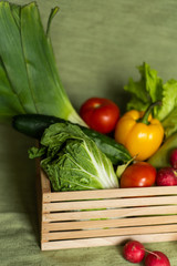Fruits and veggies in wood box with green background.