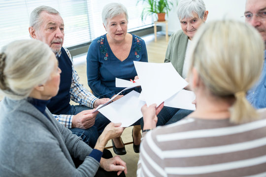 Group of seniors attending therapy group in retirement home, using sheets of paper