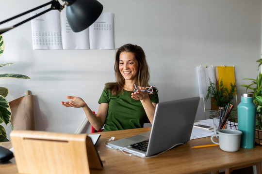 Smiling young woman gesturing while looking at digital tablet on desk in home office
