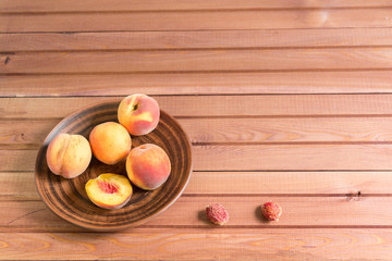 Four ripe, velvety peaches in an earthenware dish and a stone lie on a brown wooden table. Sunny