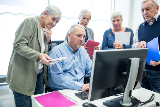 Active seniors attending computer course, watching instructor and taking notes