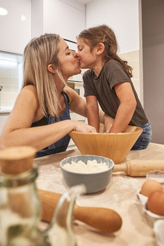 Loving Mother And Daughter Kissing While Kneading Pizza Dough In Kitchen