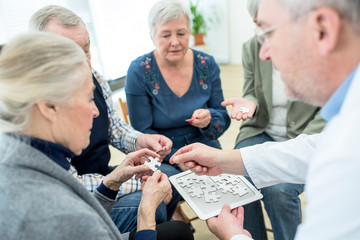 Doctor playing jigsaw puzzle with group of seniors in retirement home