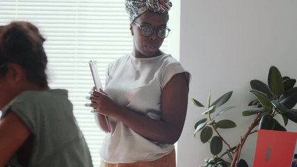 African American female teacher walking in classroom and explaining something to children while they writing in workbooks at desks during lesson in primary school