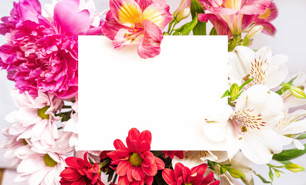 White paper card note laying in bright flowers bouquet. Romantic wedding invitation. Present for women. Birthday greeting card. Mother`s day. Space for text. Place for text. High quality photo