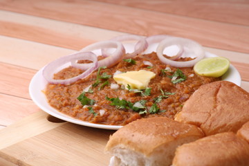 Pav Bhaji is a fast food dish from India, Thick and spicy vegetable curry, fried and served with a soft bread roll/Bun Paav and butter. Served over colourful or wooden background