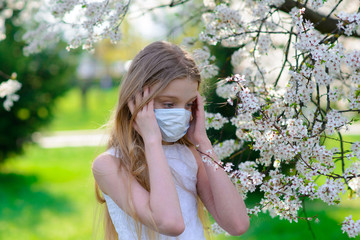 Teenager girl in medical mask in spring flowering garden. Concept of social distance and prevention of coronavirus.