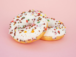 Two circle donut with white icing and choclate rainbow sprinkles on a trendy pink background. Tasty doughnutdonut, vertical view. Sweet food leftlovers. Unhealthy calorie food