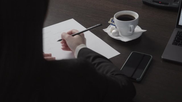businesswoman with pen and paper talks to colleague at table