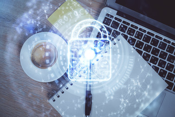 Double exposure of lock hologram drawing over study table background with computer. Concept of data security. Top view.