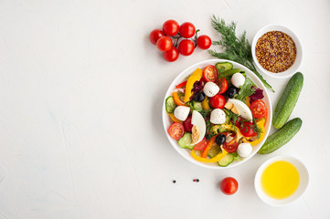 Salad of multi-colored vegetables with mozzarella and egg and ingredients from which it is made on a white concrete background. Copy space.