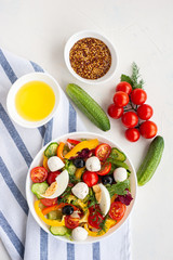 Salad of multi-colored vegetables with mozzarella and egg and ingredients from which it is made on a white concrete background. Vertical photo.