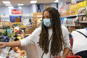 Woman with long hair shops for groceries with a face mask on during coronavirus. 