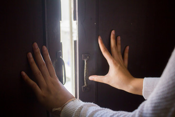 Close-up of woman’s hands pushing a vintage wooden door open to sunlight, perfect for concepts of...