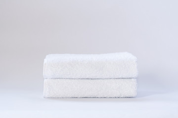 Two white neatly folded terry towels on a light background.