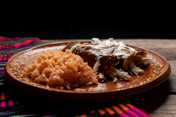 Mexican chicken enchiladas with mole sauce and rice on wooden background