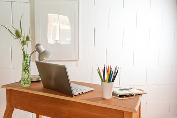 Small wooden home office desk from behind  with laptop and tools against a rough white wall, copy space