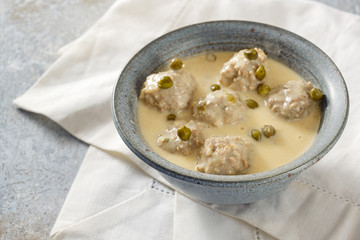Koenigsberger Klopse or boiled meatballs in a white bechamel sauce with capers, traditional Polish and German dish in a gray bowl on a white napkin, selected focus
