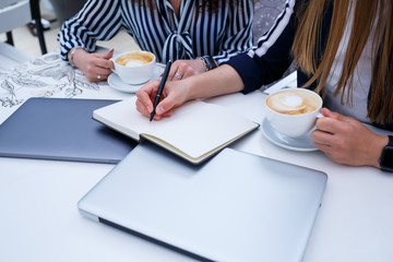 Smiling successful female workers are working together, working on a laptop on the terrace, female colleagues are busy discussing ideas, girls in a cafe at a business meeting. Business concept