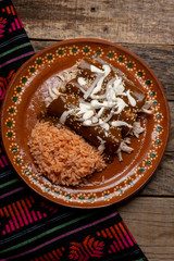Mexican chicken enchiladas with mole sauce and rice on wooden background