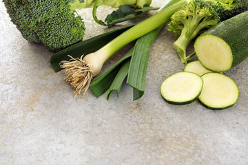 Healthy green vegetables like zucchini, leek and broccoli on a gray background with copy space