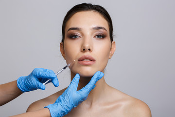 Portrait of a woman with clean skin on a gray background. Needle insertion for mesotherapy....