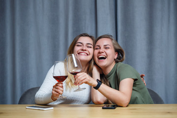 two girls of European appearance with blond hair are sitting at the table, drinking wine and laughing, relaxing at home, alcohol