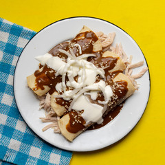 Mexican chicken enchiladas with mole sauce on yellow background