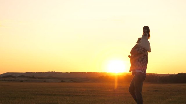 daddy carries on the shoulders of his beloved healthy child in the sun. Father walks with his daughter on his shoulders in park. child with parents walks at sunset. happy free family concept