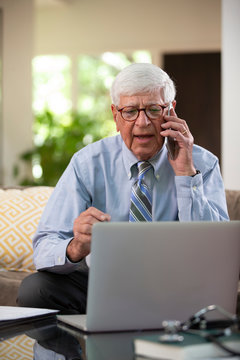 Mature Caucasian Male doctor practicing tele-medicine from his home using laptop computer, Talking to patient 