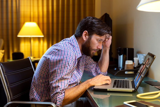 Caucasian Man Working Late In A Hotel Room, Feeling Ill So He Is Having Telemedicine Meeting With Doctor On Laptop 