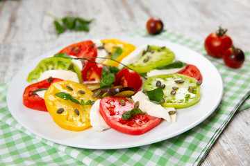 Delicious caprese salad of yellow, green and red tomatoes with cheese and fresh basil