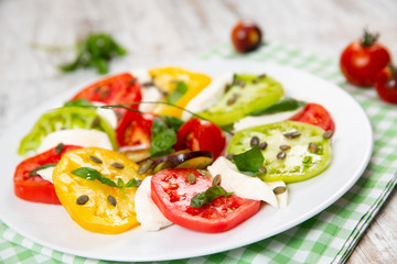 Delicious caprese salad of yellow, green and red tomatoes with cheese and fresh basil