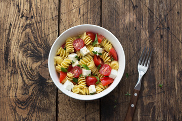 Homemade salad with pasta, tomatoes, feta cheese and spices on wooden table. simple delicious food. top view, space