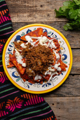 Mexican red chilaquiles with chilorio and cheese on wooden background