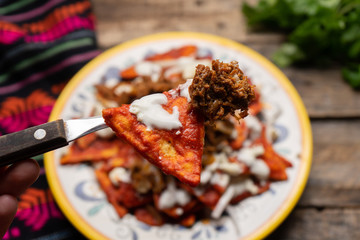 Mexican red chilaquiles with chilorio and cheese on wooden background