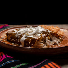 Mexican chicken enchiladas with mole sauce and rice on wooden background