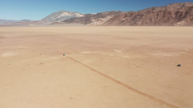 Cinematic 4K aerial around the famous moving rocks in the Death Valley on sunny winter morning. Heavy stones mysteriously moving by the bed of ancient lake bed leaving long race tracks behind, USA