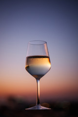 A glass of champagne on the blurred natural background of the sunset. Close-up of a glass of white wine with a copy of the space. Festive evening. Soft focus.
