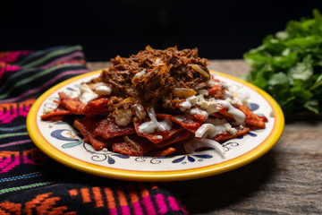 Mexican red chilaquiles with chilorio and cheese on wooden background