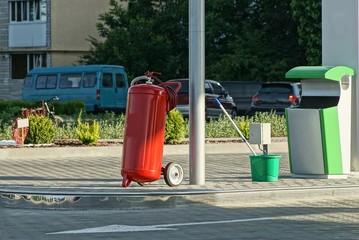 one large metal canister of red fire extinguisher on wheels stands on a gray sidewalk on the street