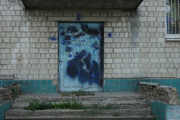 old blue wooden door with dirty black stains on the gray brick wall of the house