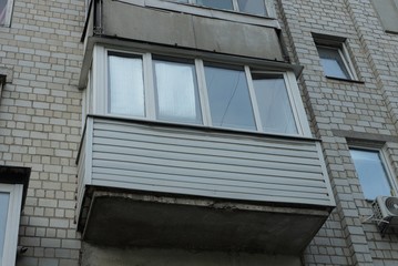 one closed gray balcony on the brick wall with windows on a large apartment building on the street