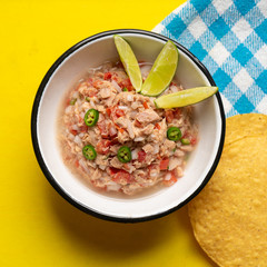 Canned tuna ceviche with chili pepper and tomato on yellow background