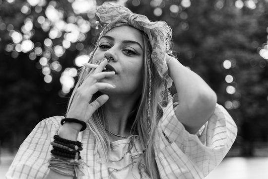 Young blonde caucasian woman standing outdoor with cigarette - Beautiful girl hold joint roll in summer day - Youth and freedom concept city life drugs cannabis legalization black and white