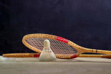 Vintage badminton racket on a black background. Badminton racket on plywood. Racket and shuttlecock on a textured black background. Vintage sport rackets with shuttlecock.