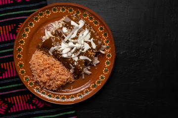 Mexican chicken enchiladas with mole sauce and rice on dark background