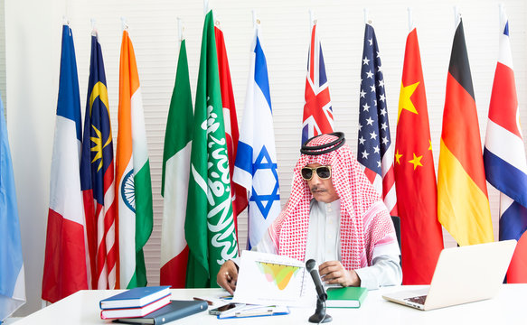 Mature Saudi confident businessman using computer with national flags cloth on poles on background, Saudi Arabia, Arabic letters mean ”There is no god but Allah And Muhammad is the messenger of Allah.