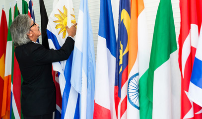 Senior businessman in suit standing by selection the flag on poles of each other country in leader room or press room. president or government statesman.