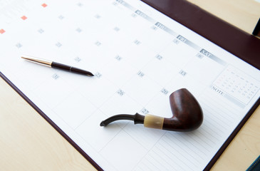 Tobacco pipe and pen on calendar yearly planner for job each day at office desk. Smoke pipe and fountain pen on planner write meeting agenda for organizer to plan timetable. Planner book and Calendar.
